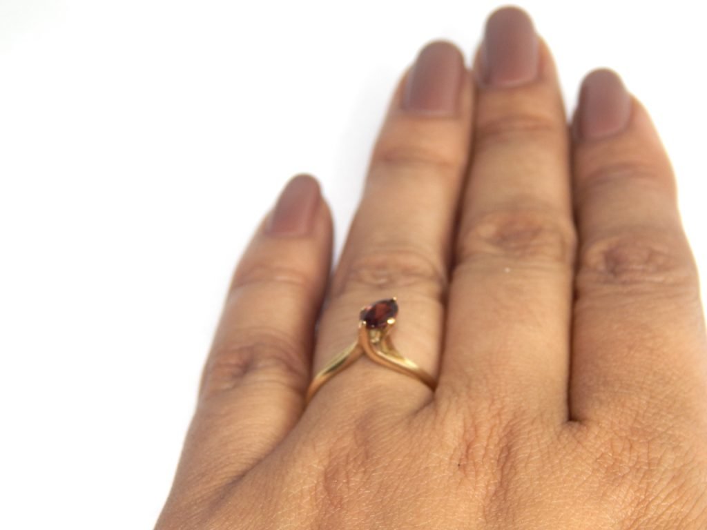 Anel em ouro 18k com desenho que parece envolver a pedra. São quatro garras diferente que seguram uma Granada Oval.